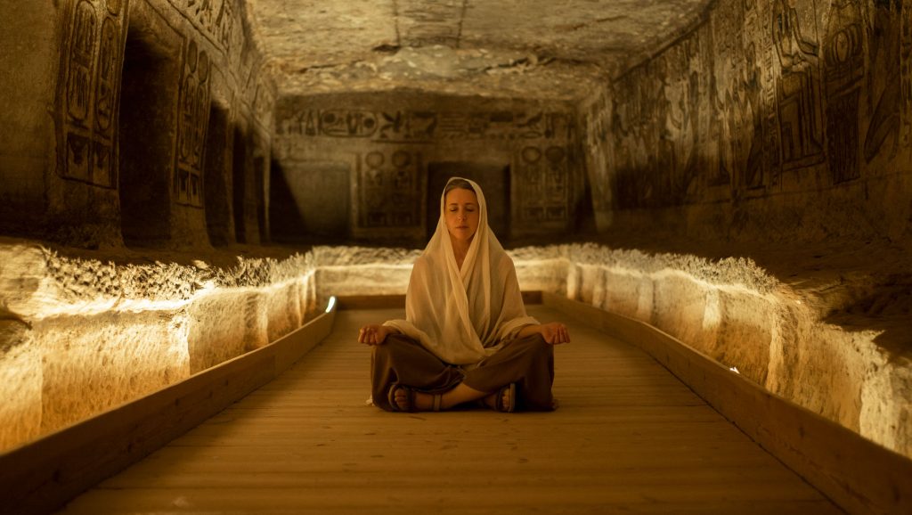 Giulia seduta in meditazione all’interno di un tempio dalle pareti incise e illuminate.