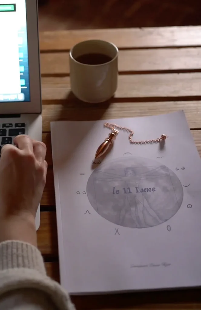 Una persona consulta il manuale delle 11 Lune su un tavolo, accanto a una tazza e a un computer.