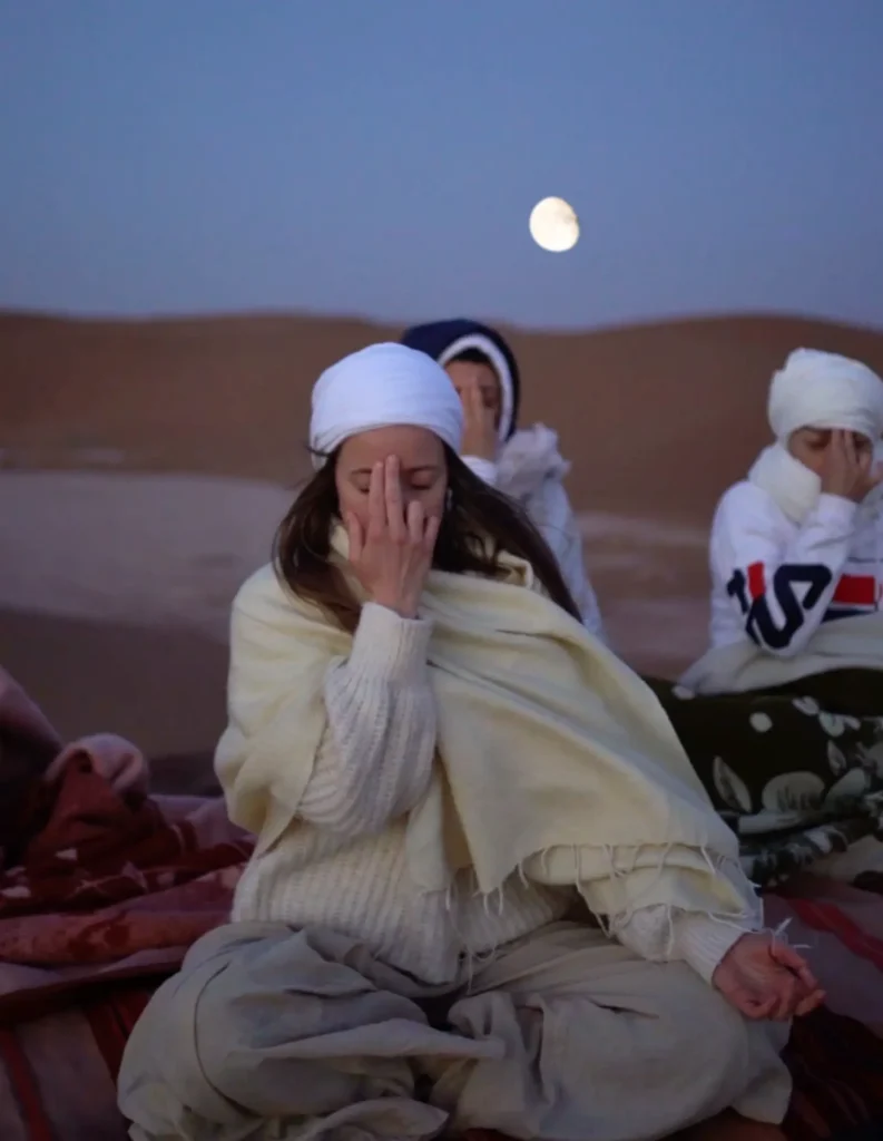 Un gruppo pratica seduto sui tappetini, nel deserto con la luna.
