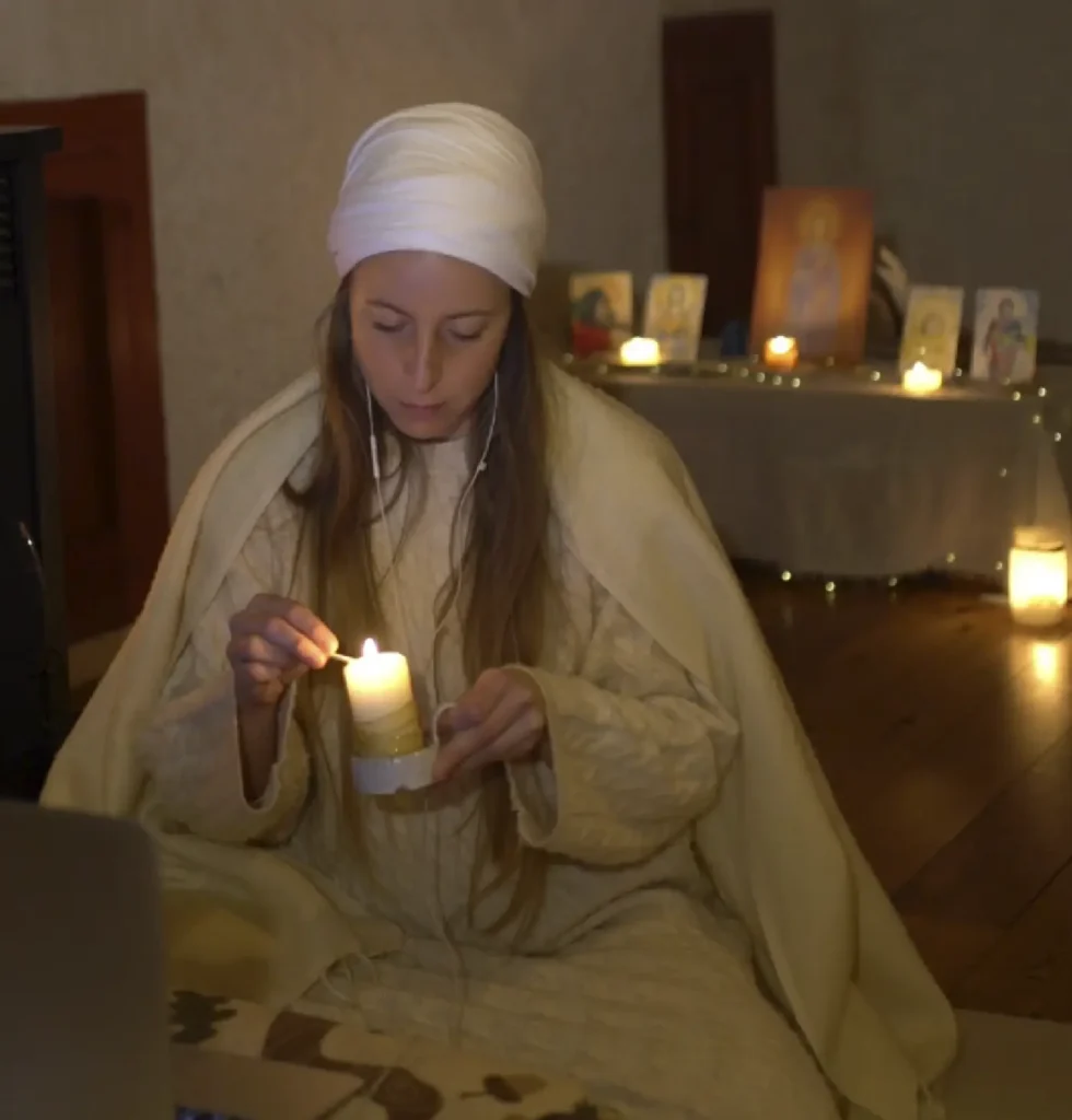 Giulia seduta in una stanza illuminata da candele, con una candela tra le mani.