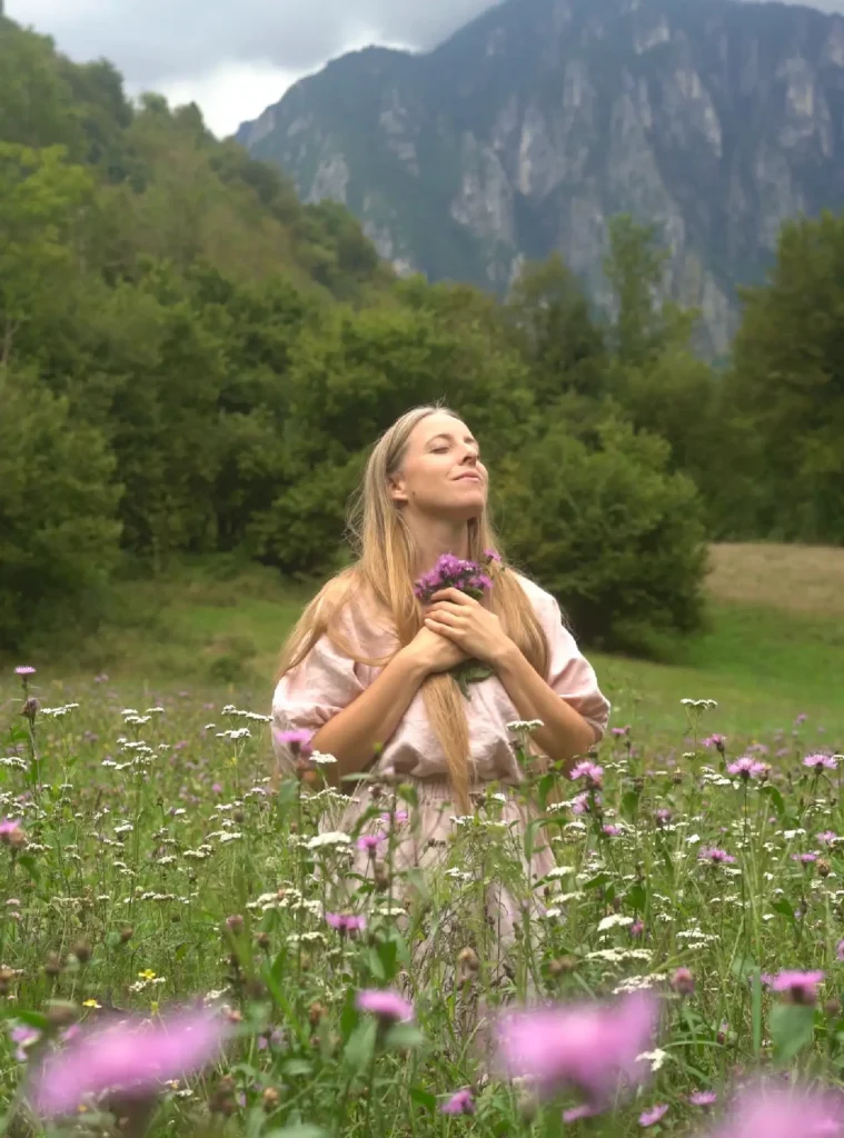 Giulia con le mani sul petto in un prato fiorito, davanti alle montagne.