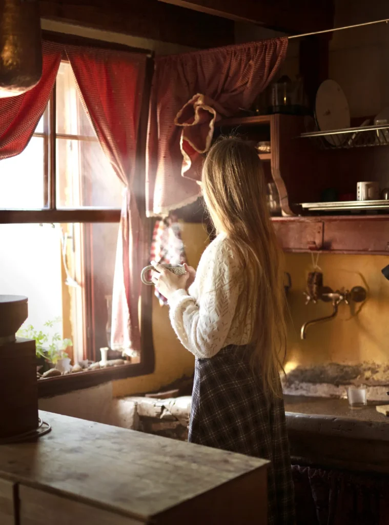 Giulia in piedi vicino a una finestra, nella luce di una cucina in legno.