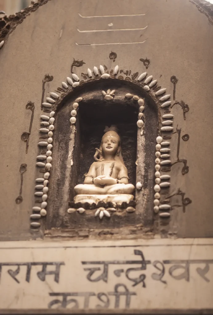 Una piccola statua in meditazione, custodita in una nicchia decorata sulla parete di un tempio.
