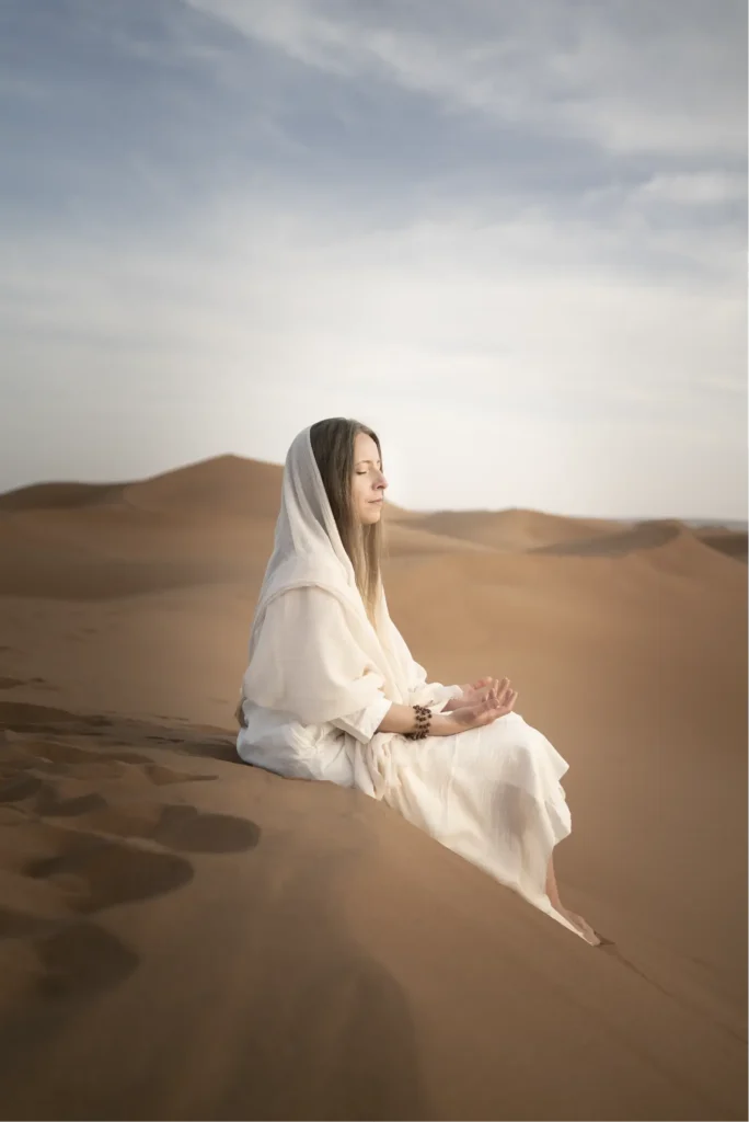 Giulia seduta in meditazione sulle dune, con uno scialle bianco sul capo.