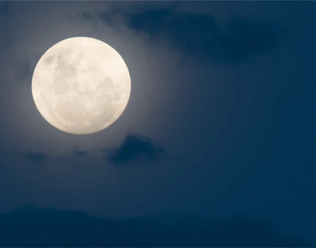 La luna piena luminosa tra le nuvole in un cielo blu scuro.